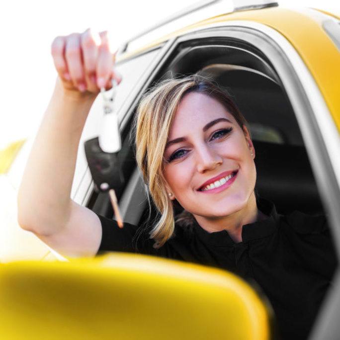 An attractive woman in the yellow car holds a car key in her hand. Rent or purchase of auto - concept.