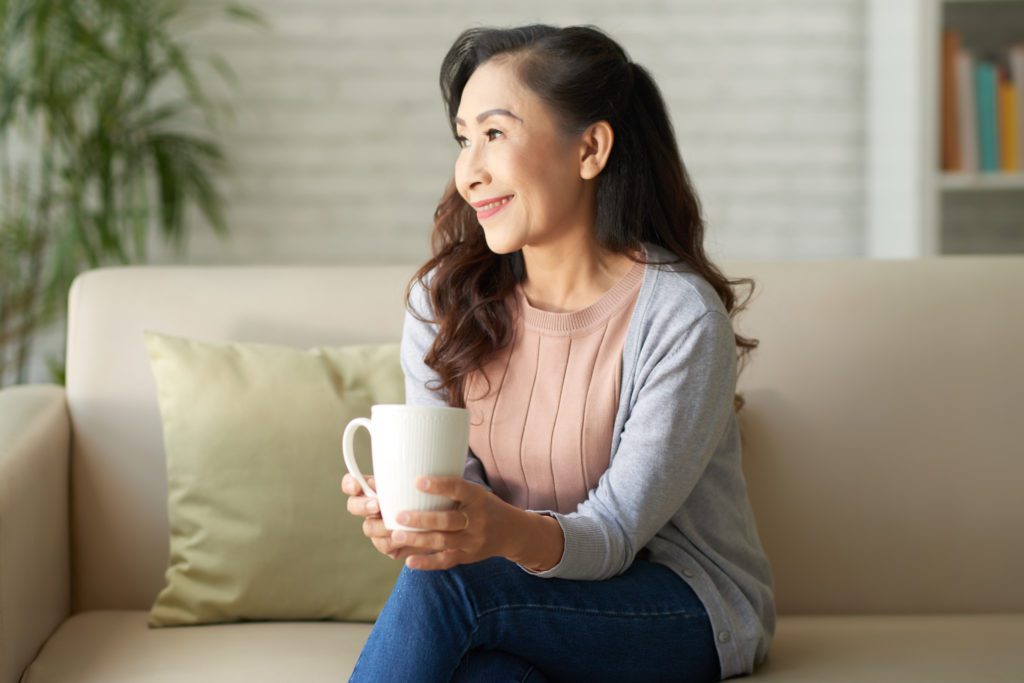 Smiling mature woman sitting on sofa and drinking coffee